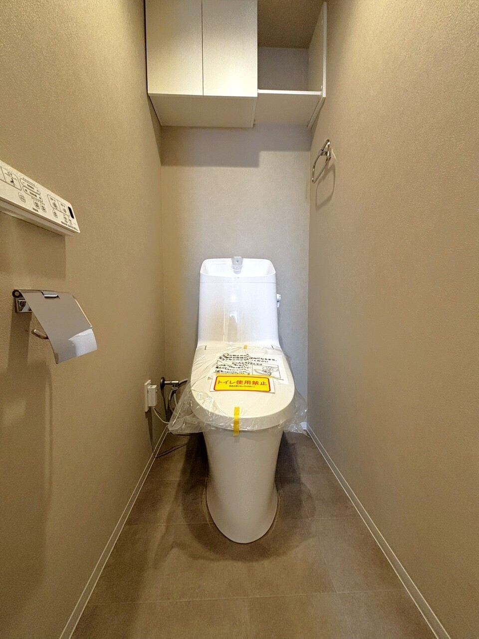 【トイレ】1年を通して快適に使用できる、温水洗浄機能付き便座が設置されています。リモコンは壁付けで操作がスムーズ。上部には吊り戸棚が設置されており、掃除用品やストック品をすっきりとしまえます。