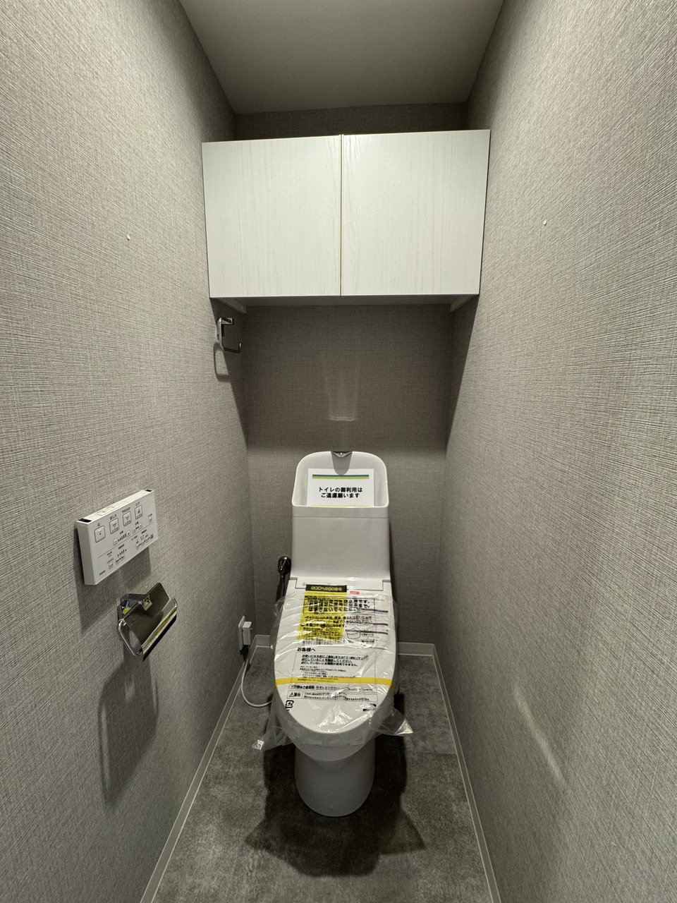 【トイレ】温水洗浄機能付き便座が備わったトイレ。操作がスムーズに行える壁付けリモコンです。背面上部には扉付きの収納が設置されています。(2025年11月リフォーム済み)