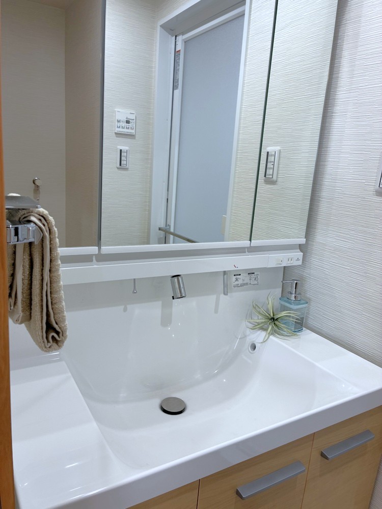 【洗面台】上からの吐水で水栓周りに水が溜まりにくく、お手入れがしやすいボウル一体型カウンター仕様の洗面化粧台。洗面ボウル下、三面鏡の裏に収納スペースが設けられており、洗面用具や日用品を収納できます。
