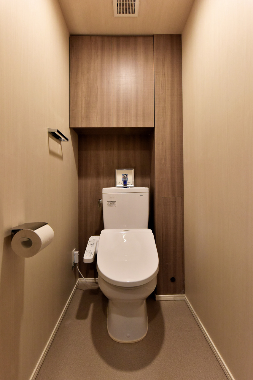 【トイレ】清潔に利用できる温水洗浄機能付きトイレです。上部には収納棚が設置されており、トイレットペーパーや掃除用品を収納することができます。