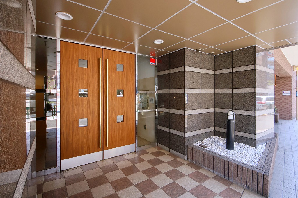 【エントランス】タイルと木目調の扉が印象的なエントランスには、防犯カメラが設置されています。日々の暮らしを安心して過ごせるよう配慮された設計です。