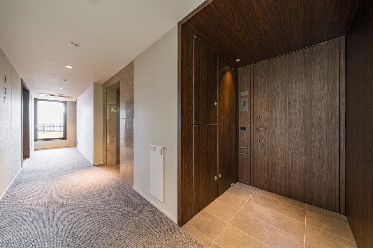 【玄関ポーチ】高級感のある木目調の玄関ドア。ダブルロック仕様で防犯面にも配慮されています。共用廊下にエレベーターが設置されており、ベビーカーや車椅子での移動もスムーズに行えます。