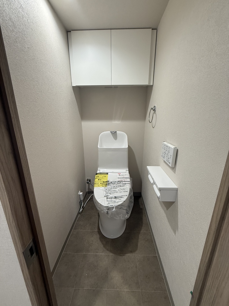【トイレ】清潔に利用できる温水洗浄機能付きトイレです。上部には収納棚が設置されており、トイレットペーパーや掃除用品を収納することができます。
