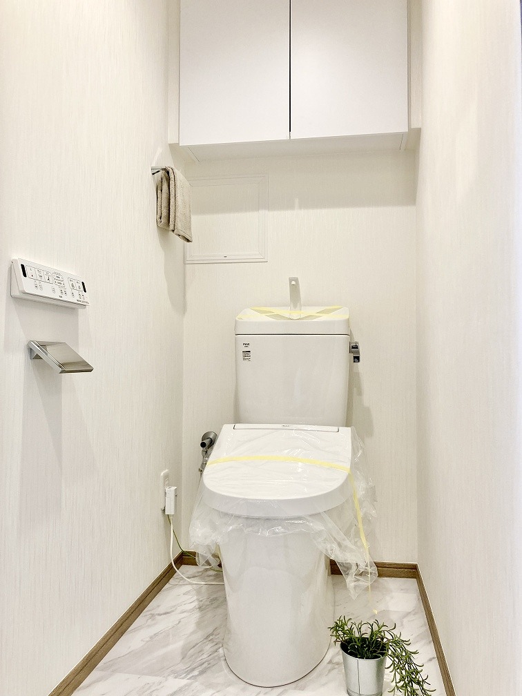 【トイレ】毎日清潔にご使用いただける、温水洗浄便座が設置されています。壁にリモコンが備え付けられているので操作がスムーズ。トイレットペーパーなどの収納に便利な吊戸棚付き。