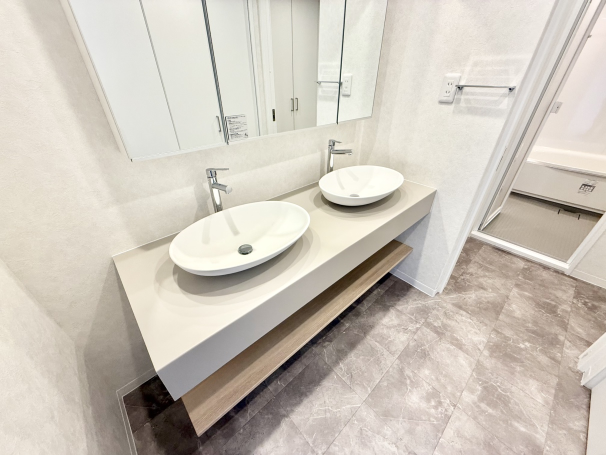 【洗面室】忙しい朝の時間帯もスムーズに身支度ができる、ダブルボウル仕様の洗面台が備え付けられています。鏡の裏やカウンター下に収納スペースがあり、化粧品類などが片付きます。