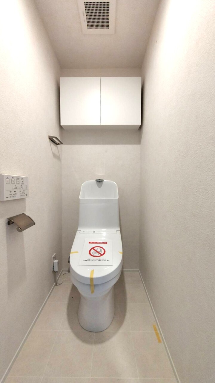 【トイレ】毎日清潔にご使用いただける温水洗浄便座が設置されています。壁にリモコンが備え付けられているので、操作がスムーズ。トイレットペーパーなどの収納に便利な吊戸棚付き。