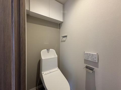白を基調とした、清潔感あふれるモダンなトイレです。温水洗浄便座や壁掛けリモコン、ペーパーホルダーが完備され、上部には便利な吊戸棚も設置アクセントクロスが落ち着いたお洒落な雰囲気を演出しています