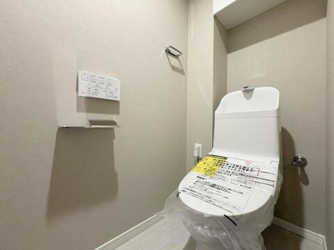清潔感のあるホワイト調でまとめられた機能的なトイレです温水洗浄便座付きのトイレで、手洗いボウルや便利な壁掛けリモコンを完備。奥には小物を置けるアクセントスペースも備わっています