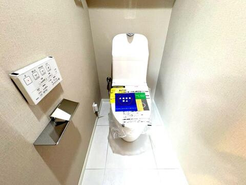 壁掛けリモコン付きの温水洗浄便座を装備した清潔なトイレ空間。落ち着いた色調のクロスで、心地よいプライベート空間に仕上がっています。