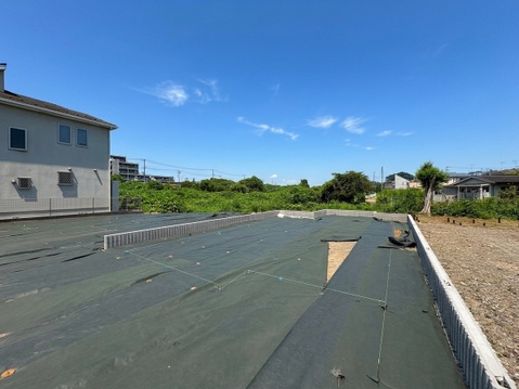 建物隣接の広い更地、周囲に住宅と田畑が見える