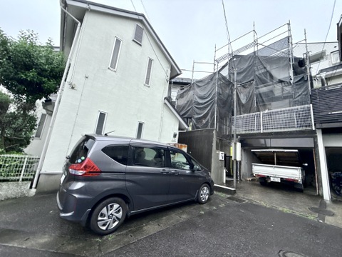 狭い敷地に建つ住宅と駐車スペースがある外観