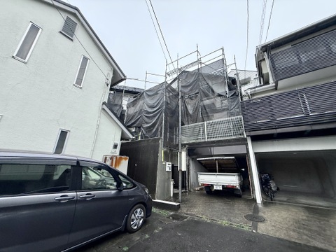 外壁工事中の住宅外観狭い通路沿いに位置
