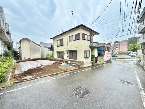住宅街の角地にある2階建ての家と空き地の様子