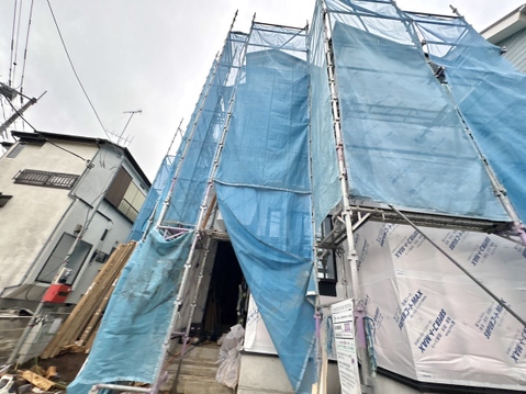建築中の建物で外装に足場と養生シートが設置されている様子です