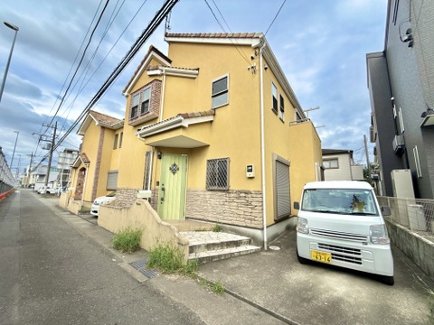 住宅街に建つ黄色い戸建て住宅と前面道路