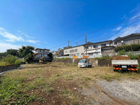 建物周辺の未整備な土地と住宅を望む外観