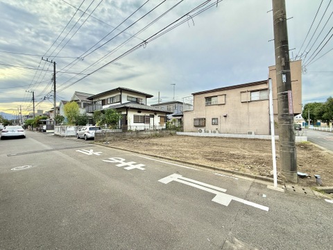 前面道路と住宅外観、周辺の電柱や住宅が見える