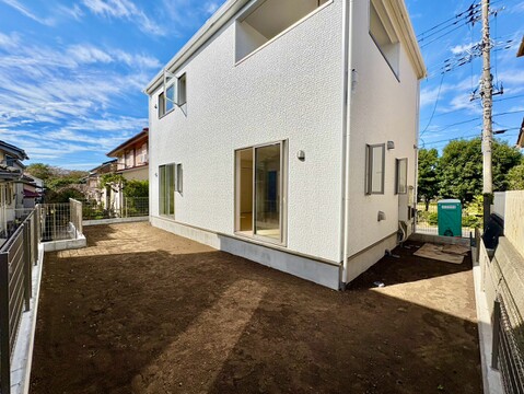 建物外観と土の庭、周囲の住宅が見える