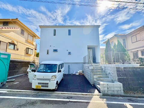 白い外観の戸建てと前面道路、駐車スペース