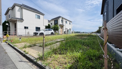 住宅地内の空き地と周囲の戸建て住宅が見える風景です