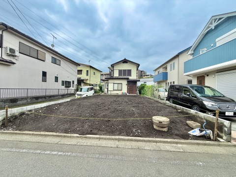 道路に面した更地の敷地周囲に住宅が立ち並ぶ