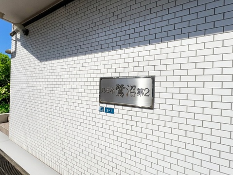 白いレンガ調の壁に設置されたマンション名のプレートです