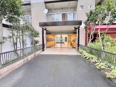 複数階建てのマンション外観、周囲に歩道と建物が並ぶ