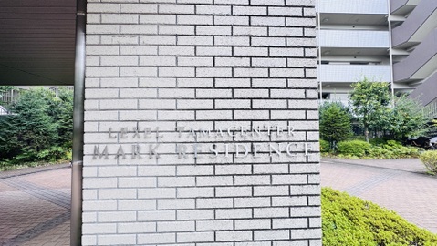 建物外壁のタイル貼りの一部と敷地内の緑地が見える外観部分