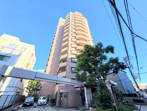 高層マンションの外観前面にエントランスと植栽が見える